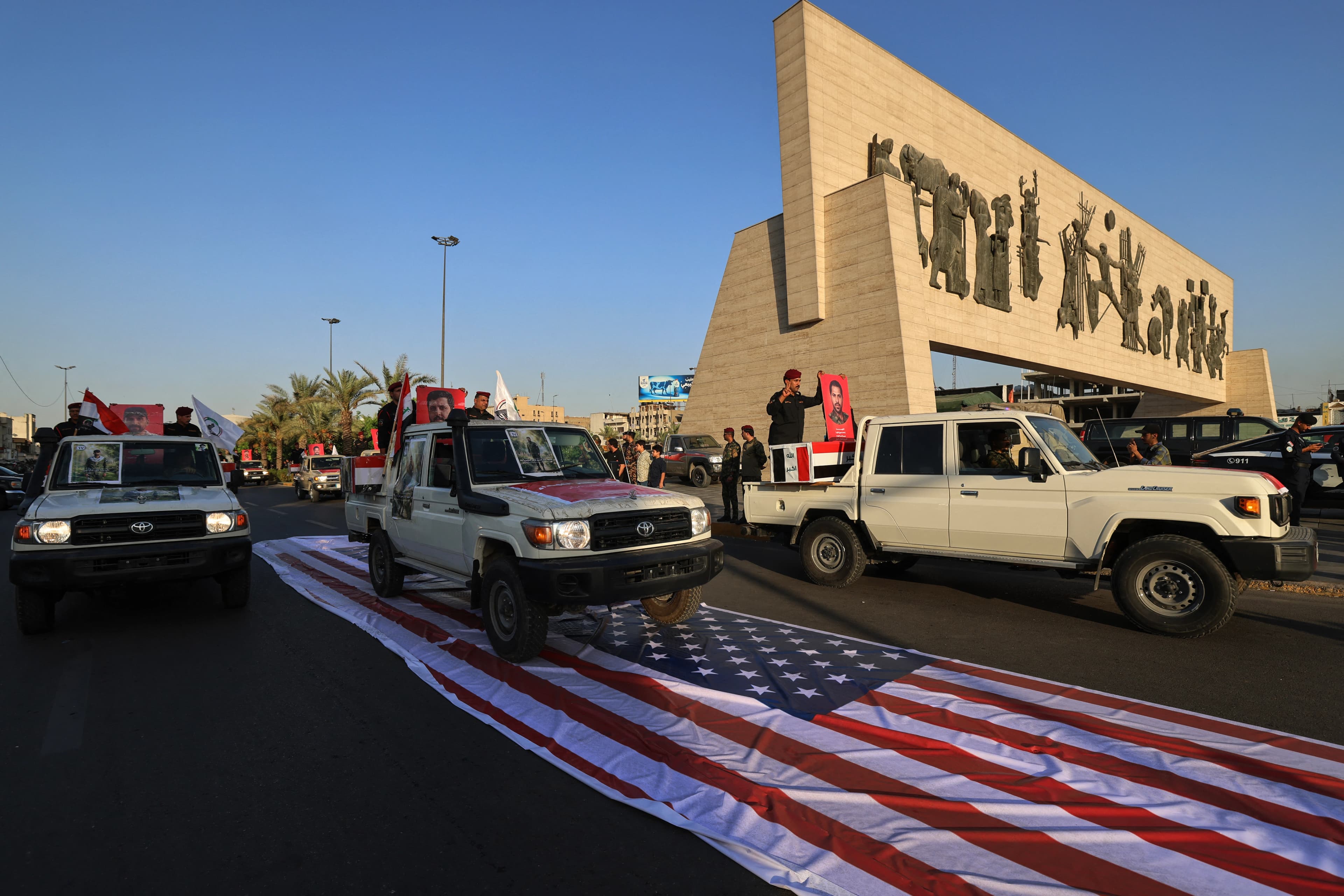 عناصر من الحشد الشعبي يمرّون بمركباتهم فوق علم أميركي خلال مراسم تشييع رمزية في بغداد-AFP